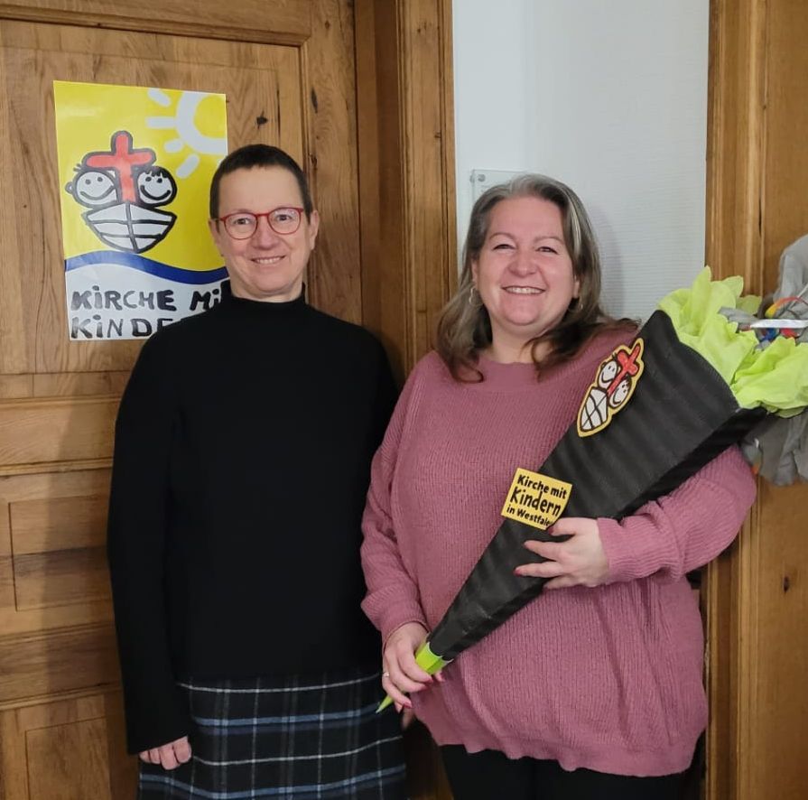 Vorsitzende Christine begrüßt Katrin als neue Mitarbeiterin im KiGo-Büro mit einer großen Schultüte.